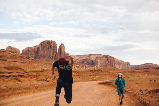Two men, one sprinting and one walking along dirt track, Monument Valley, Arizona, USA — Stock Photo