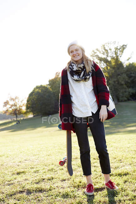 Portrait of young female skateboarder in sunlit park — Stock Photo