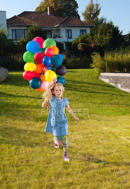 Ragazza che corre attraverso il prato con palloncini multicolori — Foto stock