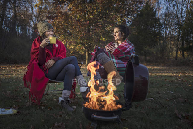 Two female friends drinking hot tea near campfire — Stock Photo