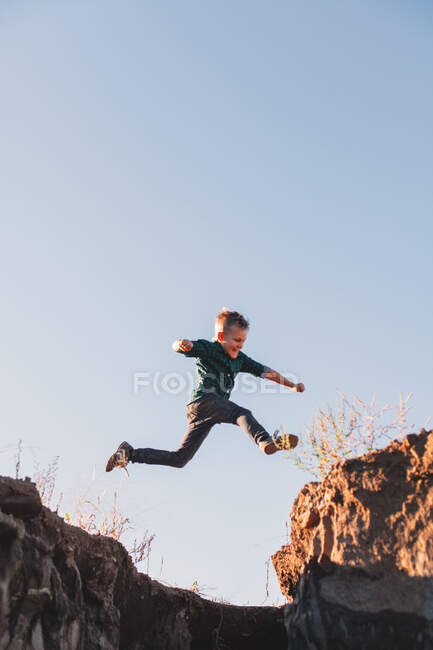 Boy jumping mid air over cliff edges — Fotografia de Stock
