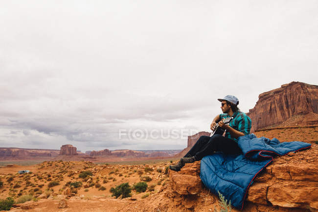 Young man sitting on rock playing acoustic guitar, Monument Valley, Arizona, USA — Stock Photo