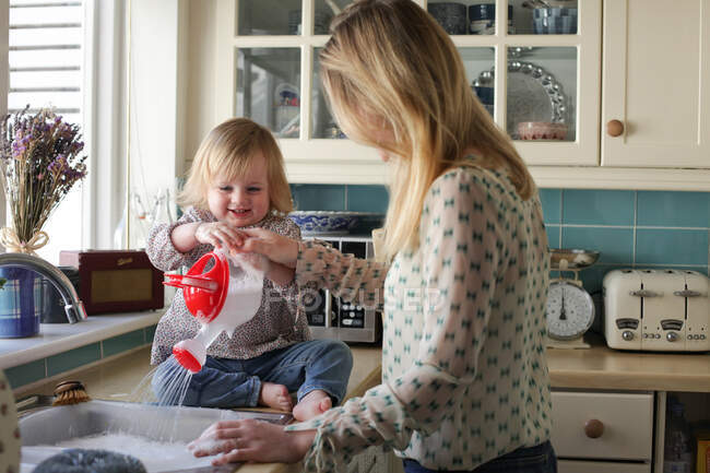 Mother washing up, daughter pouring water — Stock Photo