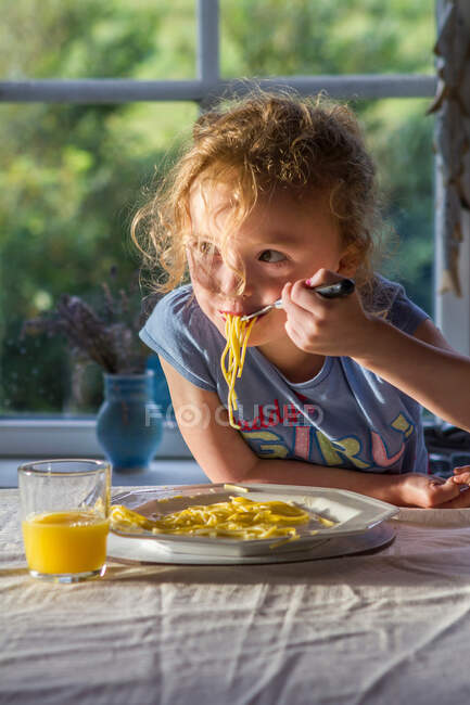 Дівчинка їсть тарілку макаронів за столом. — стокове фото