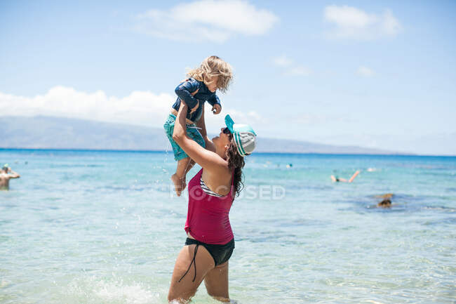 Mulher de pé no mar, levantando filho no ar — Fotografia de Stock