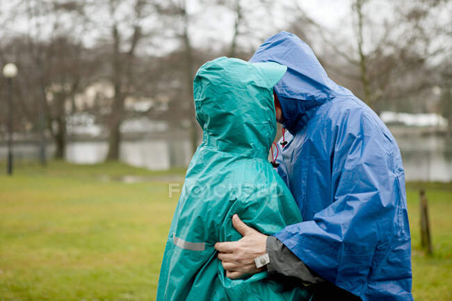 Seniorenpaar in wasserdichter Kleidung küsst sich im Park — Stockfoto