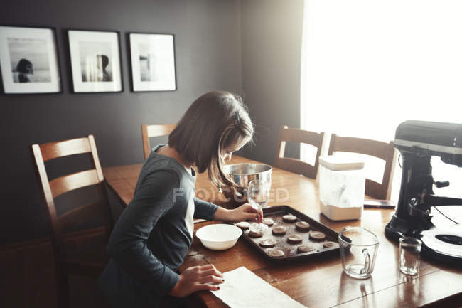Young girl decorating unbaked cookies on baking tray — Stock Photo