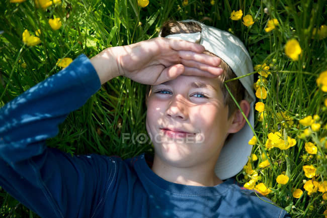 Niño acostado en la hierba con la mano en la cabeza - foto de stock