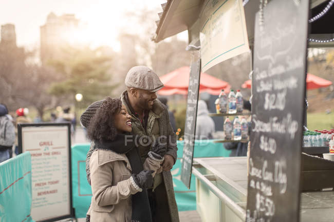 Romántico feliz pareja disfrutando de la ciudad durante las vacaciones de invierno en el parque de refresco stand - foto de stock