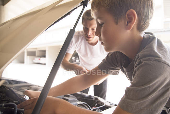 Menino aprendendo a manutenção do carro com o pai sob o capô do carro — Fotografia de Stock