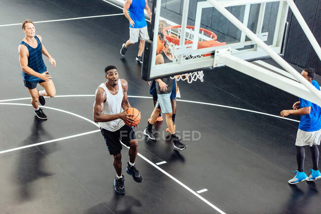 Equipo de baloncesto masculino lanzando pelota en el aro en la cancha de baloncesto - foto de stock