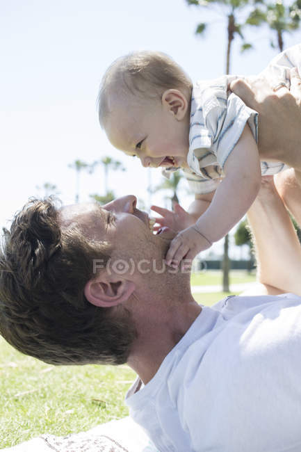 Pai segurando o filho jovem no ar, cara a cara, sorrindo — Fotografia de Stock