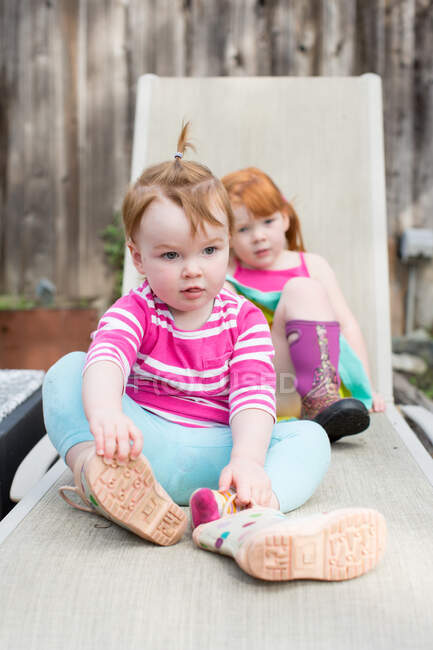 Две молодые сестры сидят на шезлонге в саду — стоковое фото