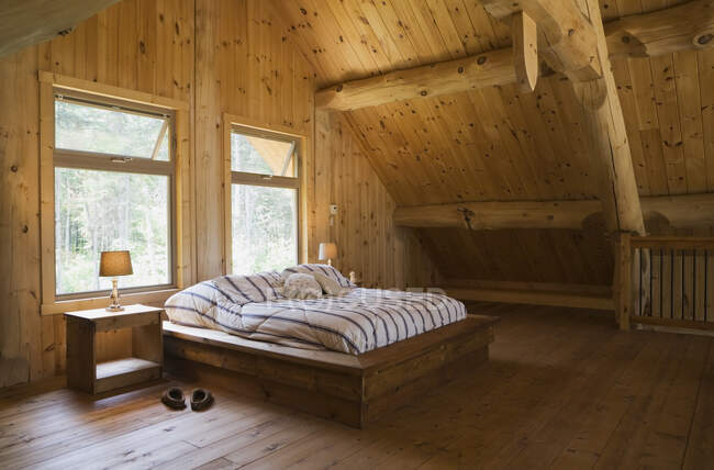 Lit King size avec cadre de lit en bois dans la chambre principale, en mezzanine à l'intérieur d'une maison en bois rond artisanale de style chalet de pin blanc de l'Est, Québec, Canada — Photo de stock