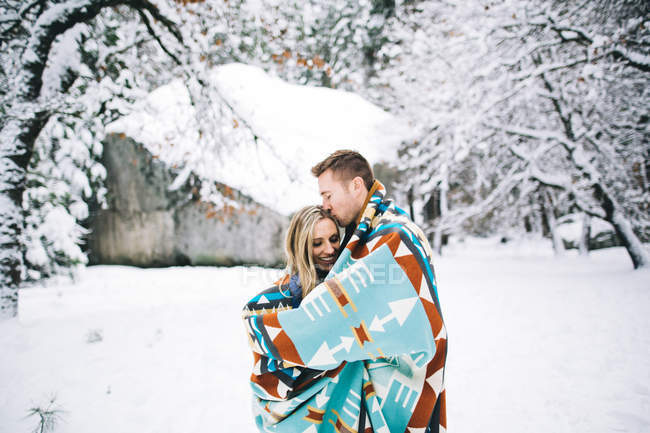 Casal em floresta coberta de neve envolto em cobertor — Fotografia de Stock