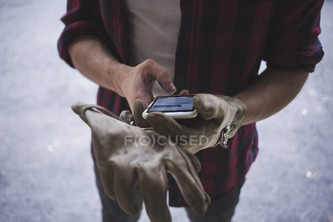 Vista recortada de ángulo alto de manos de hombres jóvenes que usan guantes protectores usando teléfono inteligente - foto de stock