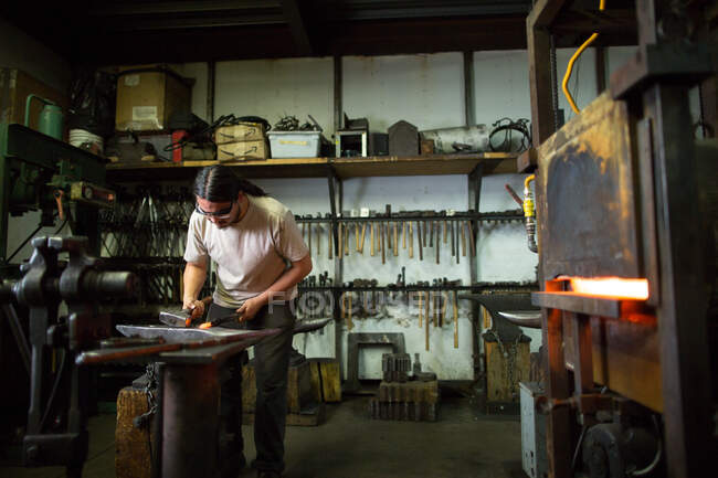 Male metalsmith hammering metal on workshop anvil — Stock Photo