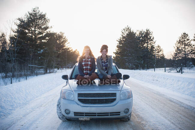 Две женщины сидят на капоте в снегу — стоковое фото