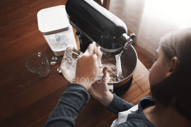 Young girl pouring ingredients into bowl of food mixer, overhead view — Stock Photo