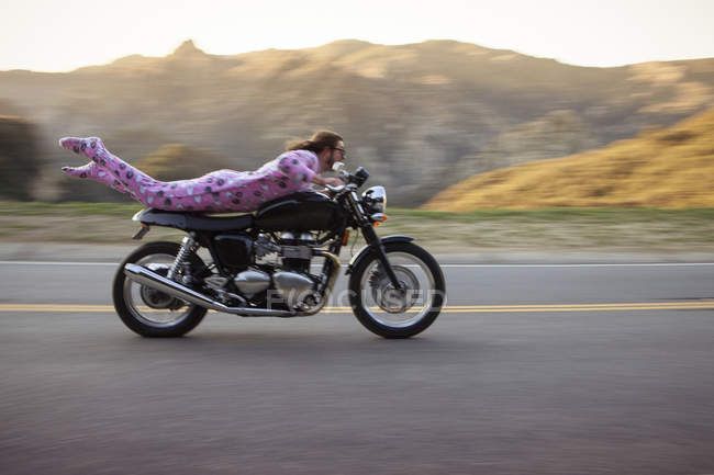 Man wearing onesie, lying on front riding motorcycle, Malibu Canyon, California, USA — Stock Photo