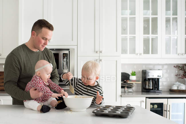 Отец и дети пекут вместе, сын кладет смесь в поднос для выпечки — стоковое фото