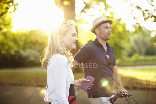 Casal com bicicleta passeando no parque iluminado pelo sol — Fotografia de Stock