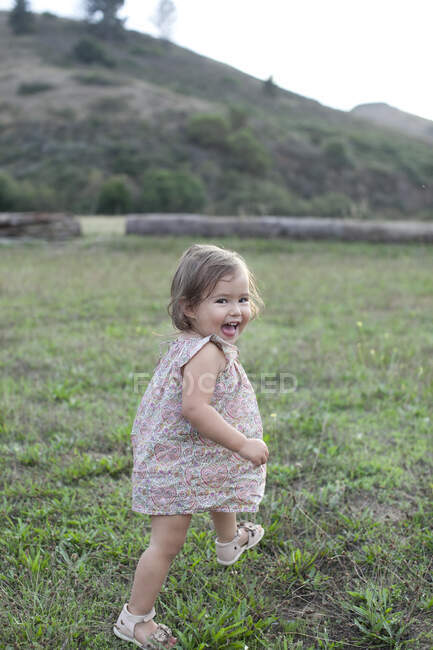 Cute female toddler running in field looking over her shoulder — Stock Photo