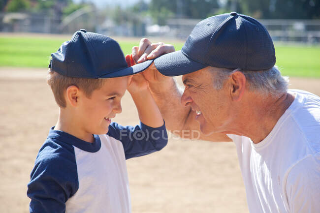 Niño y abuelo en gorras de béisbol, cara a cara - foto de stock