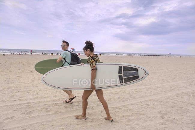Young couple carrying surfboards on Rockaway Beach, New York State, USA — стокове фото