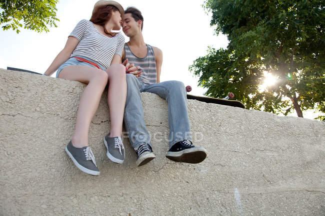 Jeune couple assis sur le mur tenant la main — Photo de stock