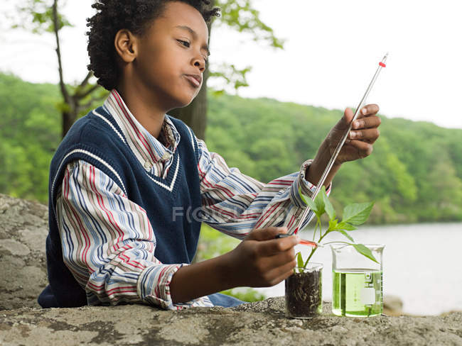 Un chico haciendo un experimento en una planta - foto de stock