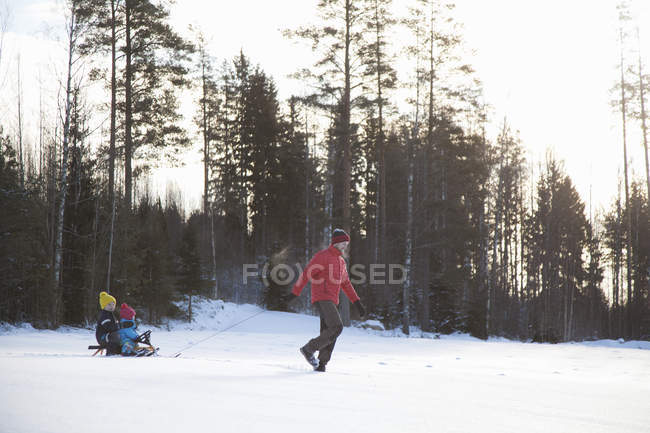 Pai puxando filhos ao longo do trenó na paisagem coberta de neve — Fotografia de Stock