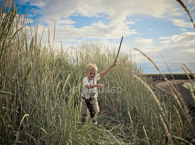 Niño jugando con la espada en el campo de trigo - foto de stock