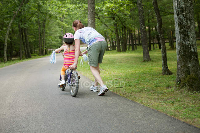Мама допомагає дочці їздити на велосипеді. — стокове фото
