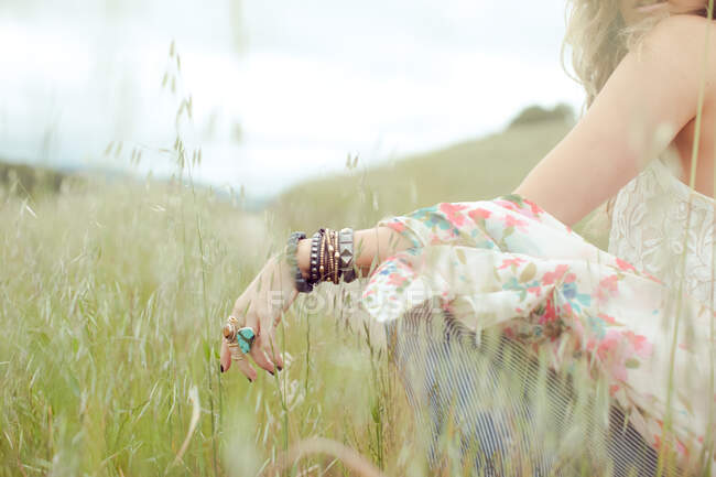 Foto cruzada de mujeres boho que llevaban globos y anillos sentados en el campo de hierba larga. - foto de stock