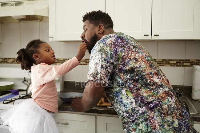 Girl feeding father in kitchen — Stock Photo