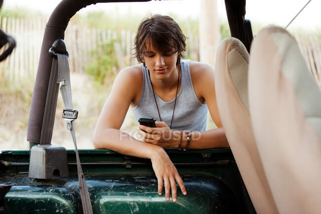 Adolescente apoyado contra jeep chequeo de teléfono - foto de stock
