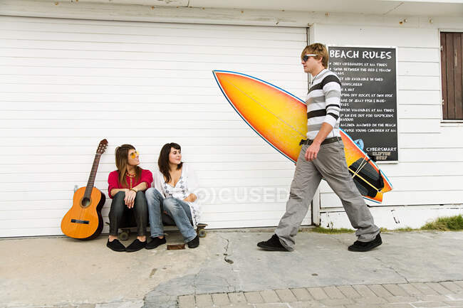 Deux filles regardant un jeune homme portant une planche de surf — Photo de stock