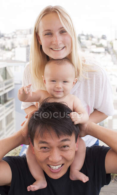 Portrait of parents with baby son on shoulders in front of window — Stock Photo