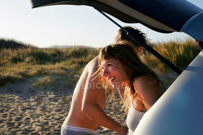 Mittleres erwachsenes Paar zieht sich am Strand aus Auto um — Stockfoto