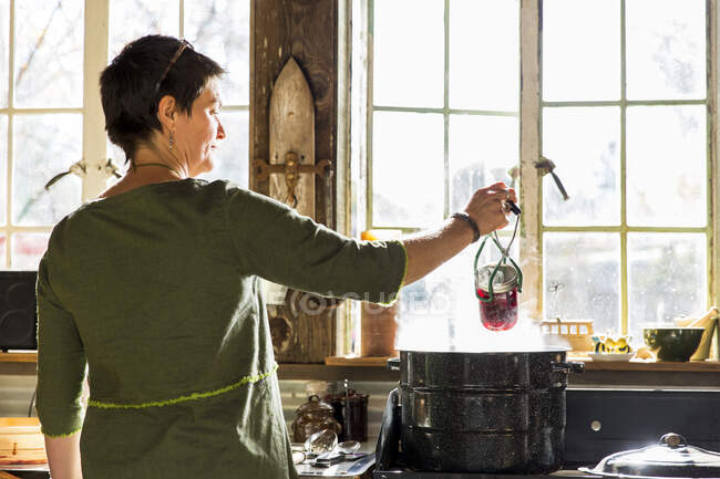 Rear view of woman removing beetroot preserves jar from steaming saucepan — Stock Photo