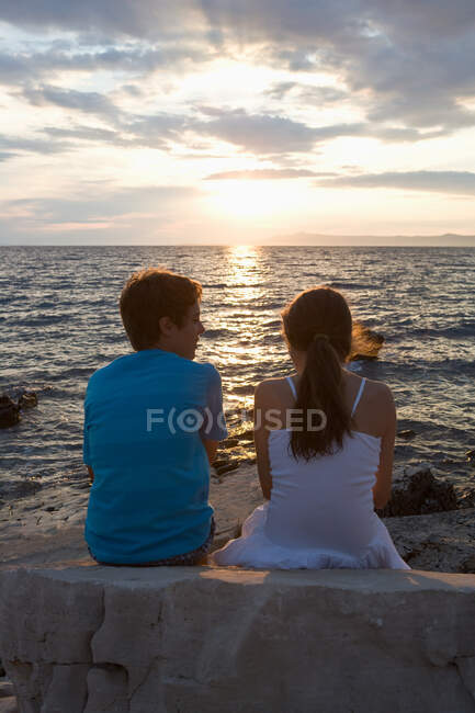 Підліткова пара дивиться захід сонця над морем — стокове фото