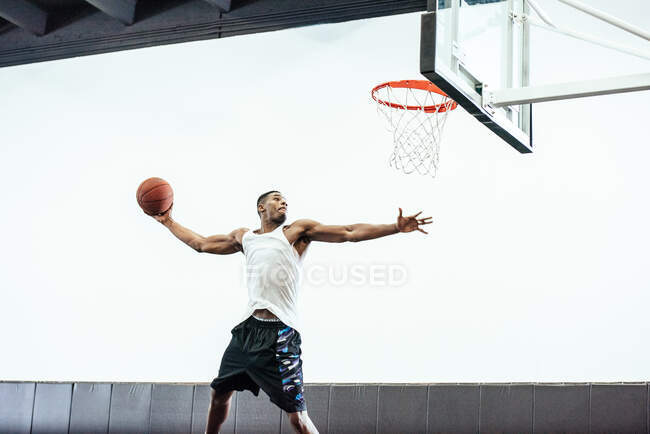 Jugador de baloncesto masculino saltando para lanzar pelota en el aro de baloncesto - foto de stock