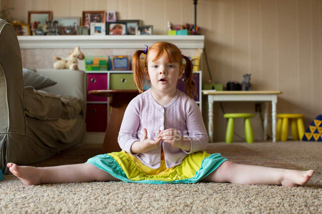 Портрет молодой девушки с рыжими волосами, сидящей на ковре, вытянутыми ногами — стоковое фото