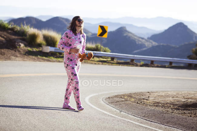 Hombre vestido de rosa onesie caminando por la carretera llevando osito de peluche, Malibu Canyon, California, EE.UU. — Stock Photo