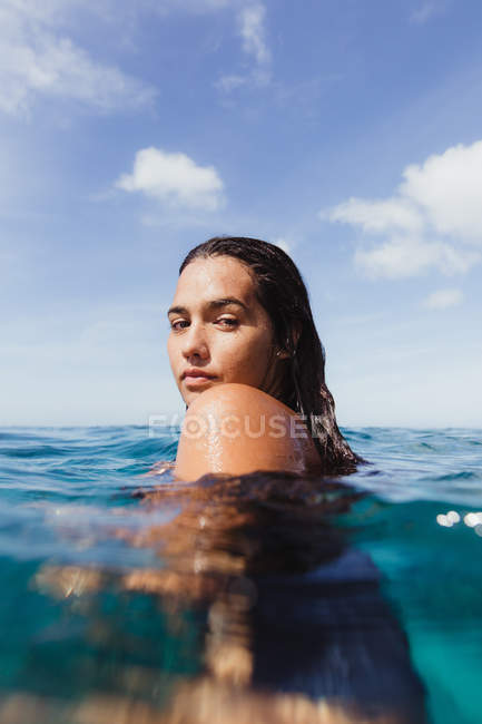 Femme en mer regardant par-dessus l'épaule à la caméra, Oahu, Hawaï, États-Unis — Photo de stock