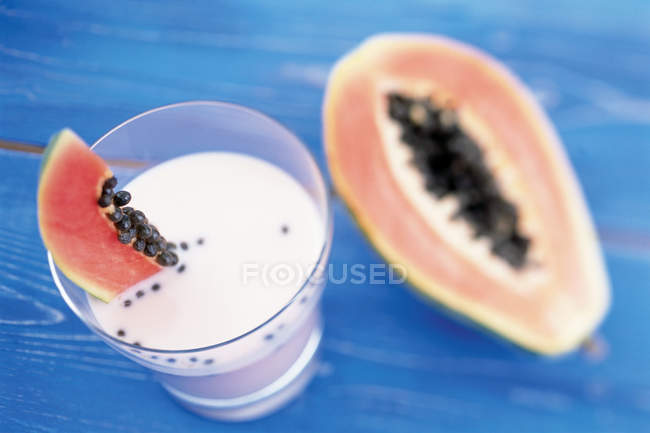 Fruit milkshake glass and halved papaya on table — Stock Photo