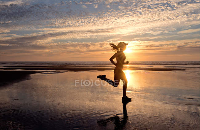 Frau läuft bei Sonnenaufgang am Strand — Stockfoto
