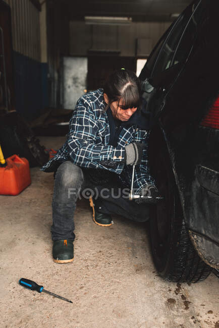 Frau wechselt Reifen ihres Fahrzeugs in Werkstatt — Stockfoto