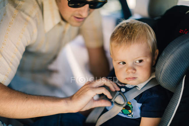 Padre assicurando giovane figlio in seggiolino auto — Foto stock